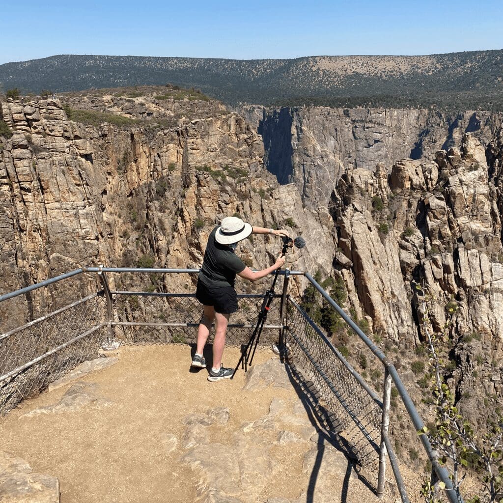 A woman taking pictures with a large steep canyon in the background