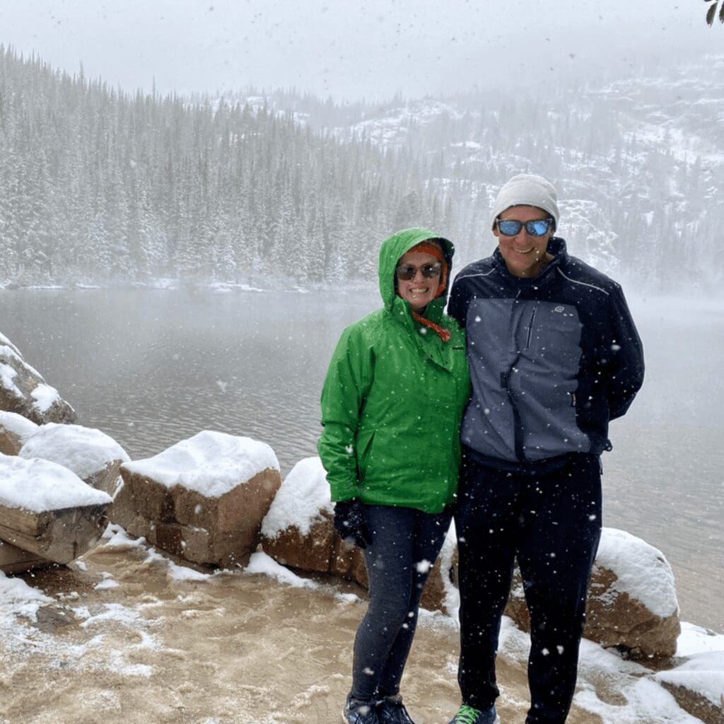 A man and a woman standing by a lake with snow falling