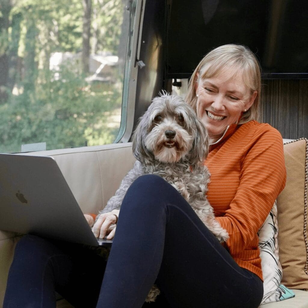A woman sitting on a couch with a computer and a gray dog in her lap
