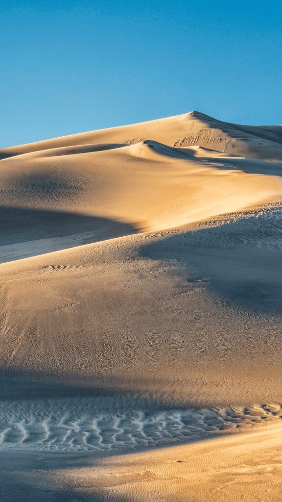 vast areas of sand dunes with people in distance walking over the hills