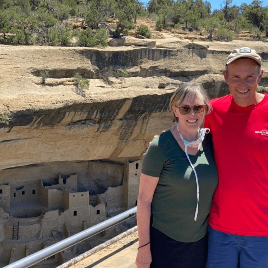 A man and woman standing in Mesa Verde with ancient cliff dwellings in background