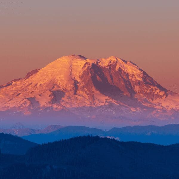 blue foreground of rolling hills with Mount Rainier in background under a red sky