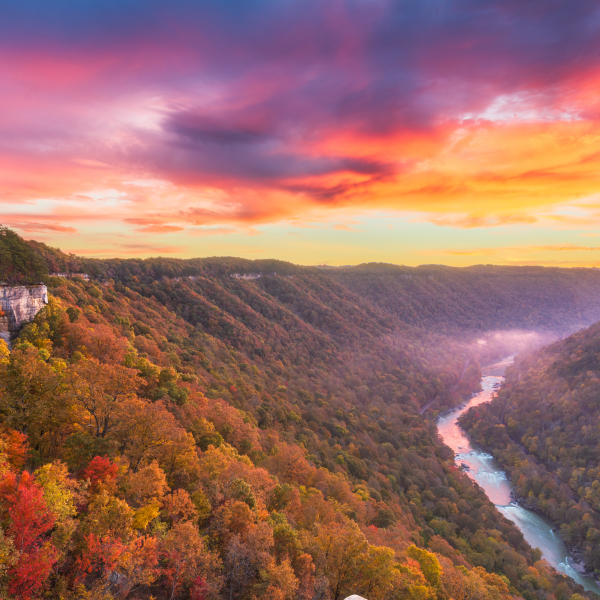 a beautiful sunrise over new river gorge with autumn trees to the sides and fog over the river below