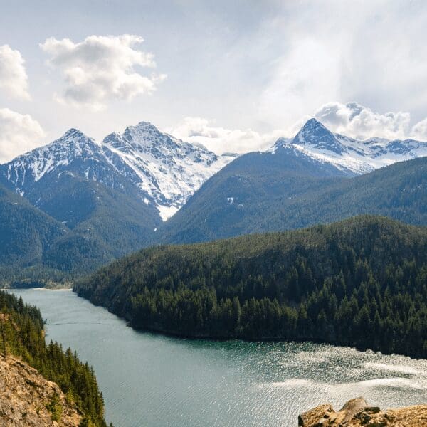 Snow capped mountains in the rear with the lake in the foreground. the picture is from a spring day in North Cascades National Park