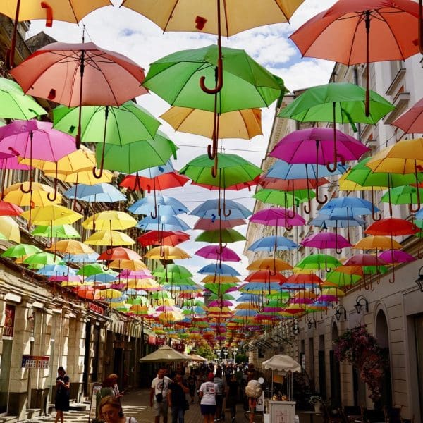Umbrellas of different colors hanging overhead a walkway between buildings in Timisoara