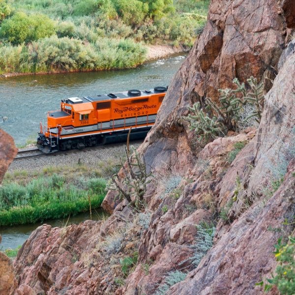 orange train passing by mountain below the Royal Gorge Bridge