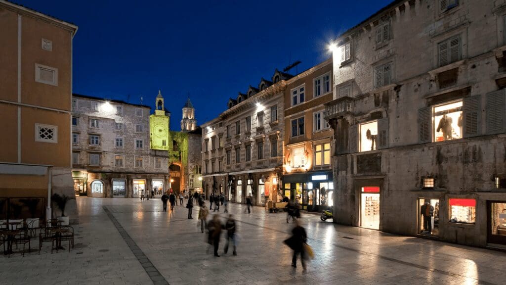 a night view of the square with old buildings and people strolling