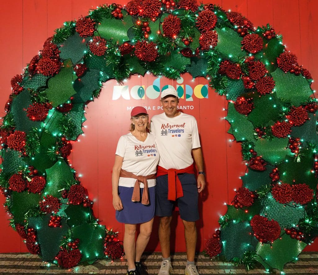 John and Bev standing in a giant Christmas wreath with a red background