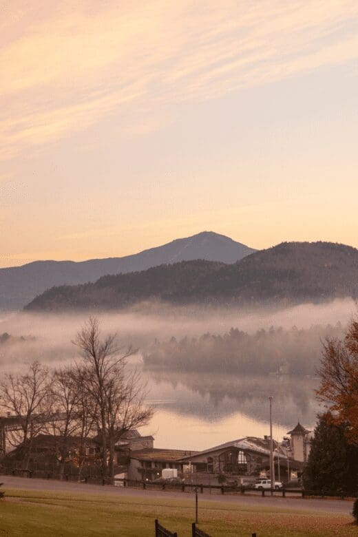 Morning view of fog over Lake Placid with mountains in the background and a cottage in the foreground