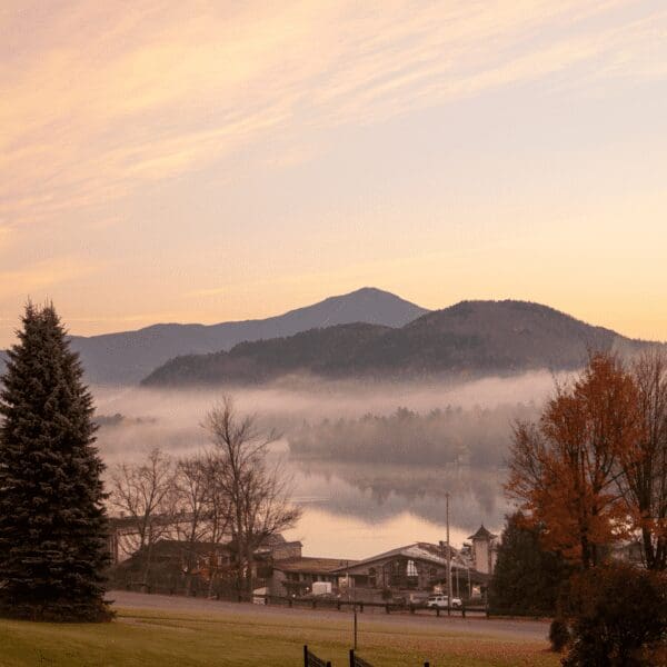 Morning view of fog over Lake Placid with mountains in the background and a cottage in the foreground