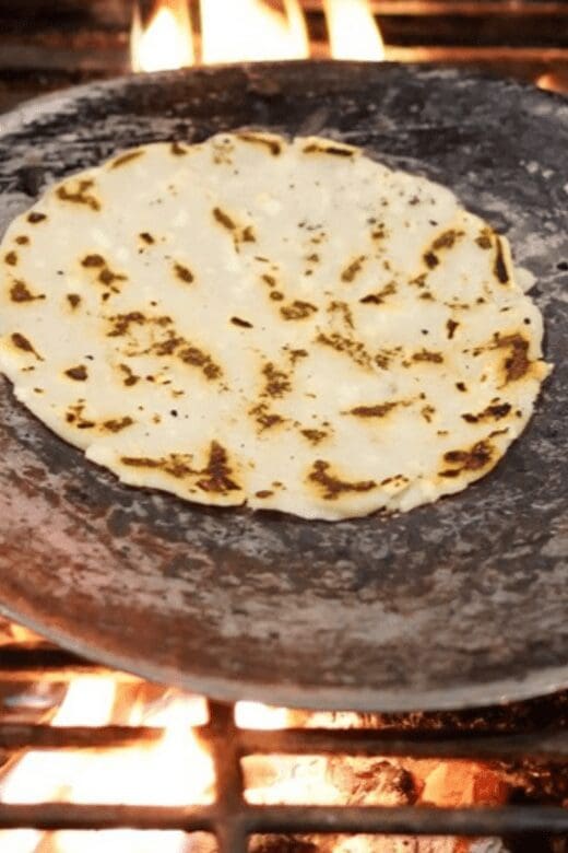 Corn tortilla in a metal skillet over open flames on a grill
