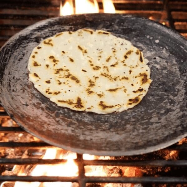 Corn tortilla in a metal skillet over open flames on a grill