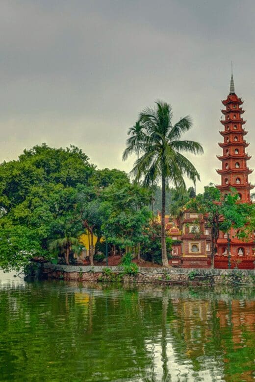 View of an ancient temple surrounded by tall lush green trees and water.