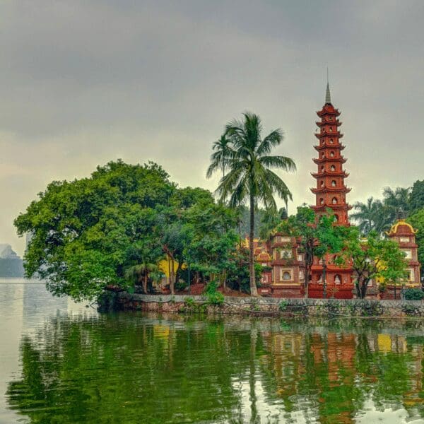 View of an ancient temple surrounded by tall lush green trees and water.