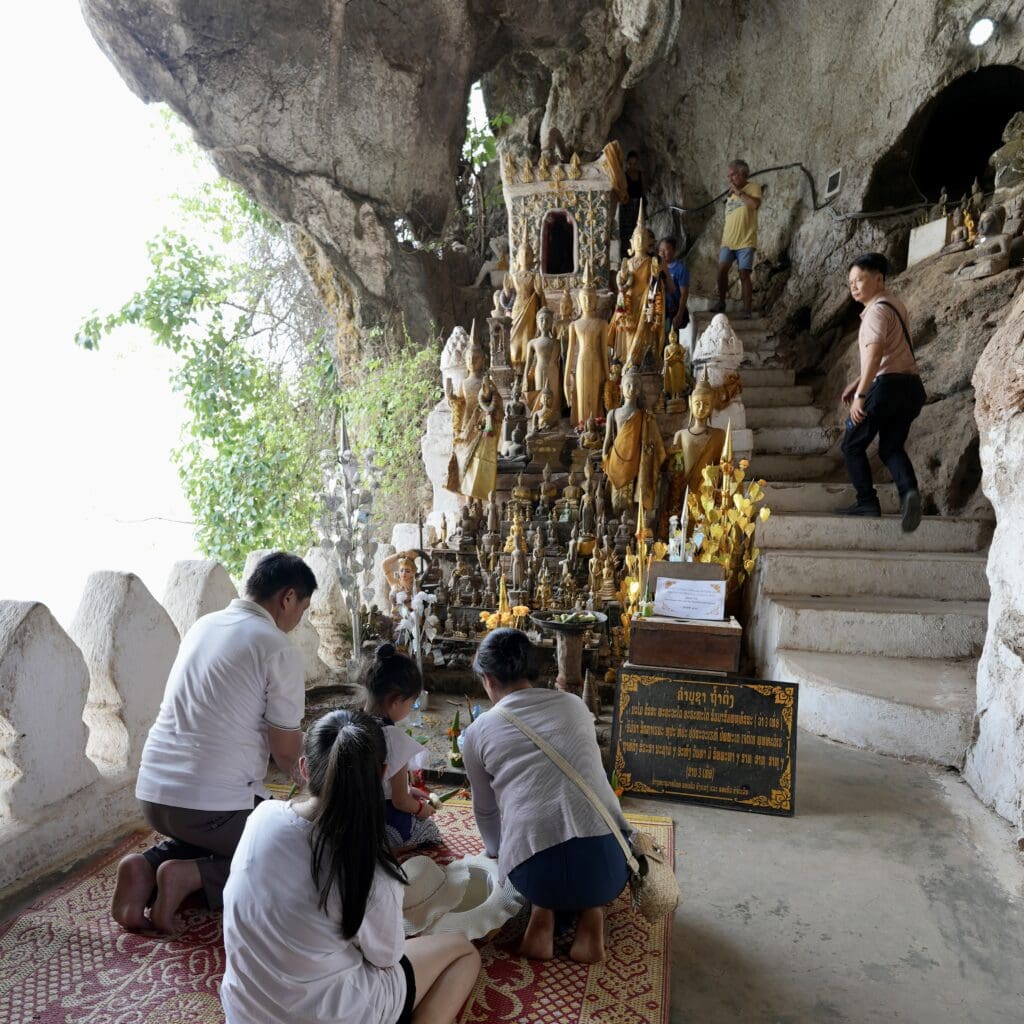 people praying near Buddha statues in a cave
