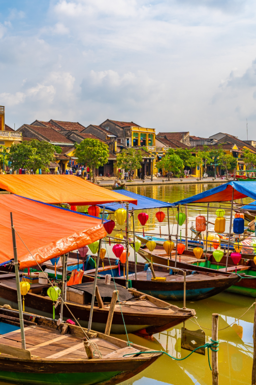 Wooden boats with colorful lanterns docked in water along the city of Hoi An.