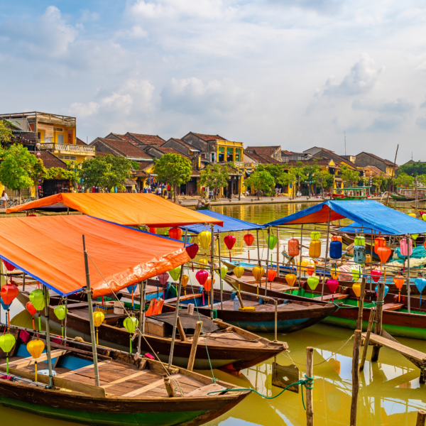 Wooden boats with colorful lanterns docked in water along the city of Hoi An.