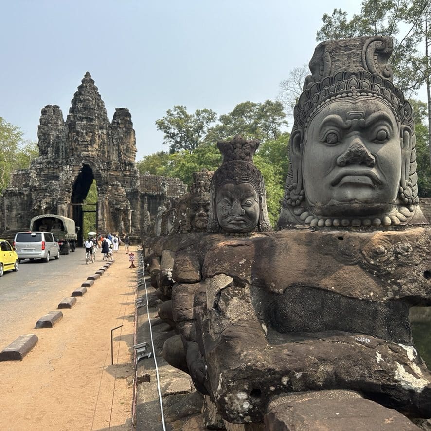 Tonle Om gate with stone statues lining roadway to the tall stone gate