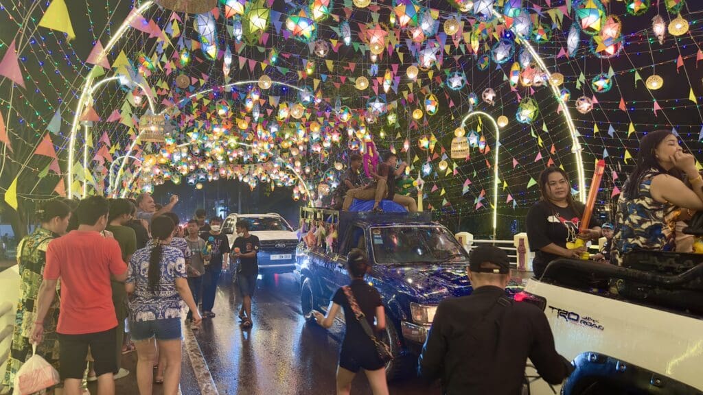 celebration with many people and cars going over a bridge decorated with banners and flags