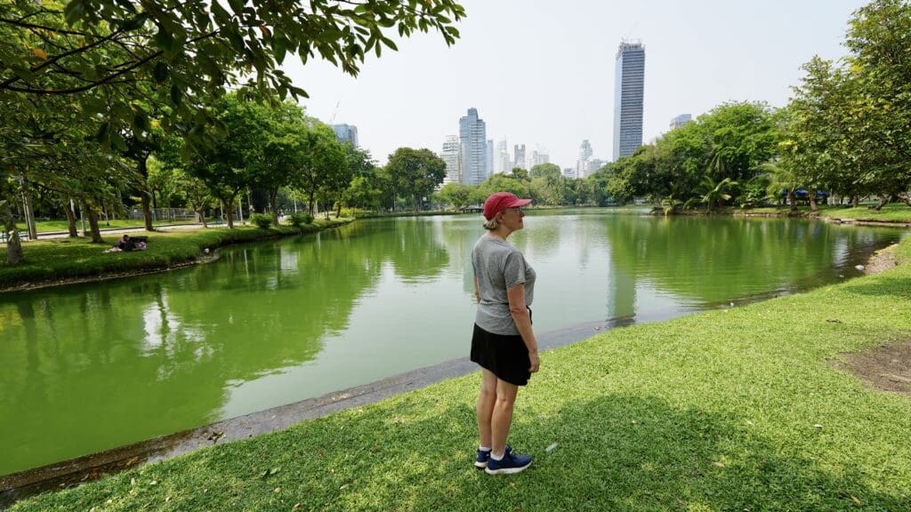 woman standing by a large pond in a park with city skyline in background