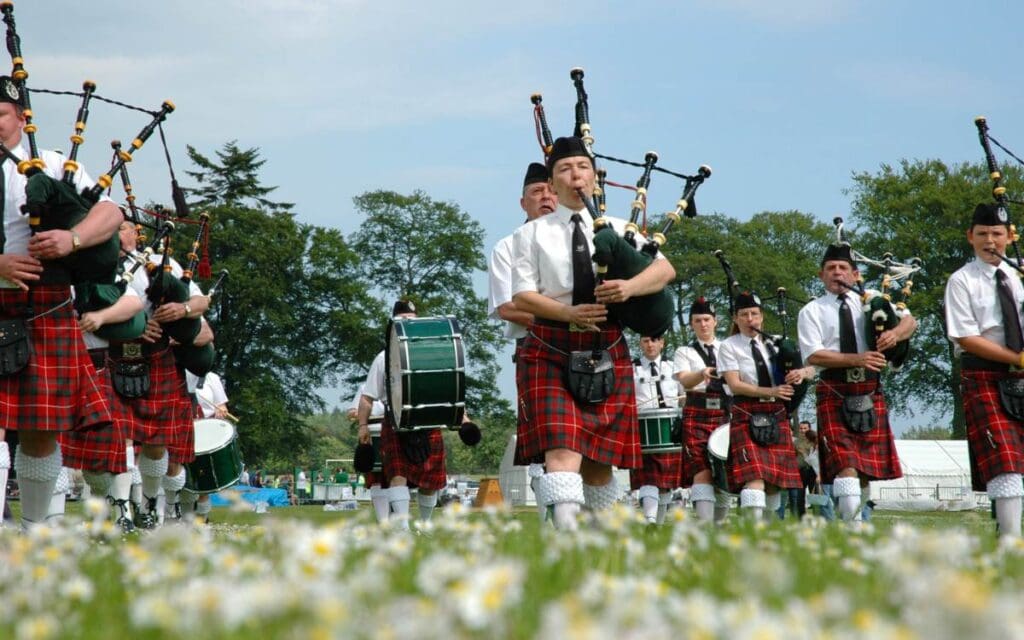 men in red kilts playing bagpipes in a field of flowers