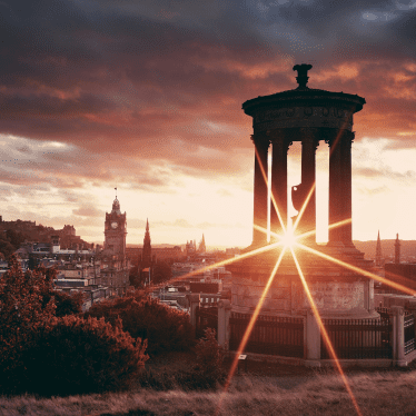 Calton Hill view of the city of Edinburgh with the sun shining through at sunset.