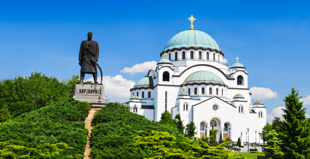 A white dome church in Belgrade, Serbia with a green dome and a statue in front
