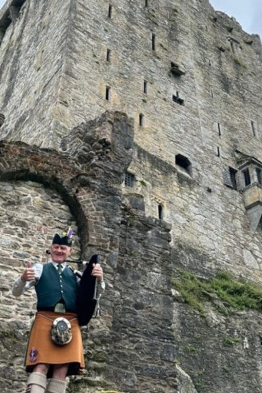 Man playing bagpipes standing in front of a castle in Ireland