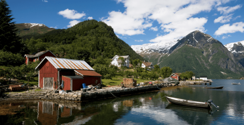 View of a red barn along the water with fjords in the background in Norway