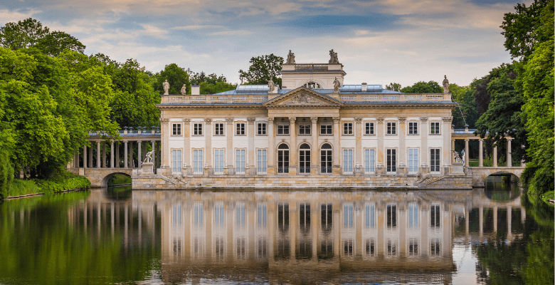 Large stone building with windows behind a lake surrounded by trees